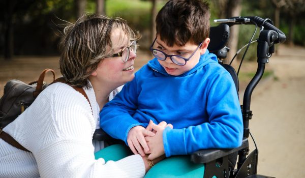 Boy in a wheelchair enjoying a walk outdoors with his mother.