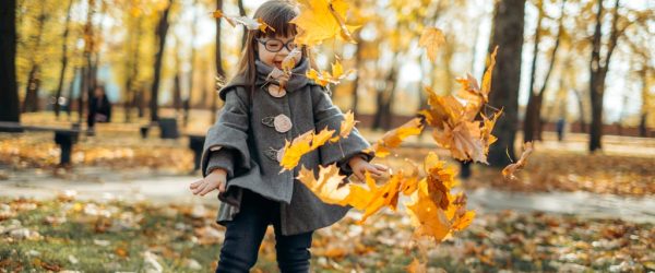 A girl with down syndrome in fashionable coat and stylish eyeglasses tossing bright foliage.