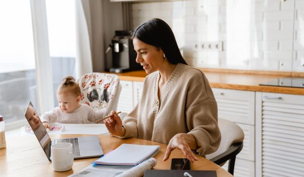 Young mother working with laptop, with her baby next to her.